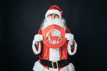 Man dressed as Santa Claus holding a forbidding reindeer traffic sign, on black background. Christmas concept, Santa Claus, gifts, celebration.の写真素材
