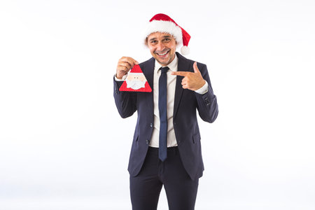 Businessman dressed in suit, tie and Christmas hat of Santa Claus, smiling, on white background. Christmas celebration concept.の写真素材
