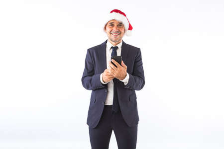 Businessman dressed in suit, tie and Christmas hat of Santa Claus, smiling, on white background. Christmas celebration concept.の写真素材