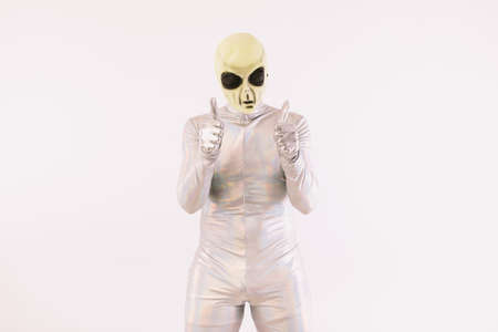 Person wearing silver suit and green alien mask with thumbs up, on white backgroundの写真素材