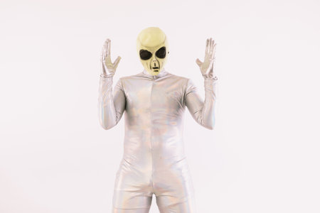Person dressed in silver suit and green alien mask raising hands in surprise, over white backgroundの写真素材