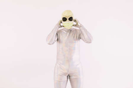 Person dressed in silver suit and green alien mask, putting on a green mask to avoid being infected by a virus, on white backgroundの写真素材