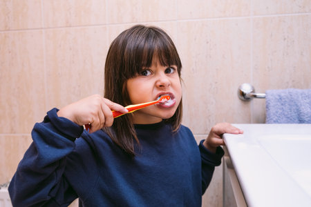 Little girl in dark blue sweatshirt, brushing her teeth, in the bathroom. Tooth brushing, hygiene and childhood concept.の写真素材