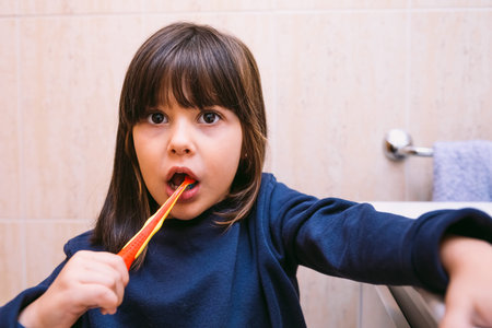Little girl in dark blue sweatshirt, brushing her teeth, in the bathroom. Tooth brushing, hygiene...