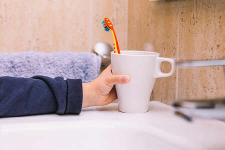 Detail of the arm of a little girl in the bathroom, clutching her cup with the toothbrush inside. Tooth brushing, hygiene and childhood concept.の写真素材