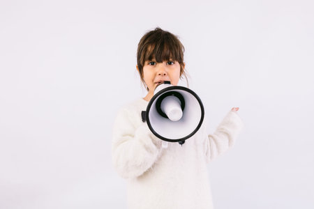 Little black haired girl wearing white sweater with bow tie, speaking through a white megaphone.