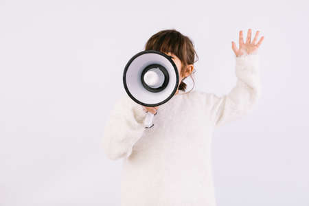 Little black haired girl wearing white sweater with bow tie, speaking through a white megaphone.の写真素材