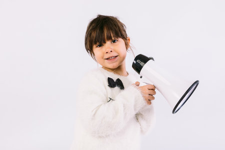 Little black haired girl wearing white sweater with bow tie, speaking through a white megaphone.の写真素材