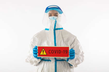 Nurse doctor in personal protective equipment and latex gloves holding a red sign that reads: 'COVID-19'. Coronavirus, pandemic and health concept.の写真素材