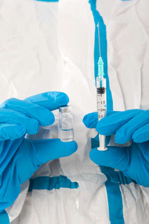 Medical nurse in PPE and latex gloves holding a syringe with a covid-19 vaccine. Coronavirus, pandemic and health concept.の写真素材