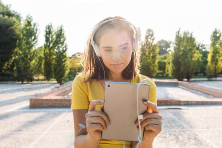 Young blond hair girl wearing yellow t-shirt, smiling and looking at her tablet, with the sun behind. Technology, lifestyle and relaxation conceptの写真素材