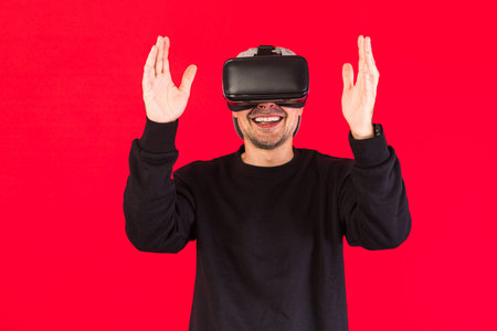 Man in cap dressed in black wearing Virtual Reality glasses smiling while touching something...