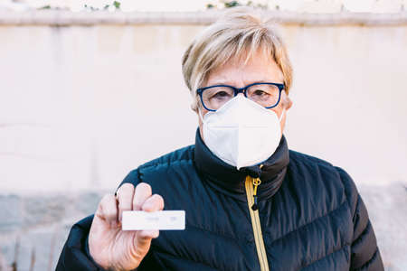 Elderly lady on the street, wearing a white mask, with a negative antigen test. Concept covid-19, ihu, delta, omicron, detection test and pandemic.の写真素材