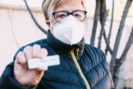 Elderly lady on the street, wearing a white mask, with a negative antigen test. Concept covid-19, ihu, delta, omicron, detection test and pandemic.の写真素材