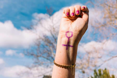 Fist of an older woman with purple painted nails, with the sky in the background, with the female symbol painted. Concept of women's day, empowerment, equality, inequality, activism and protest.の写真素材