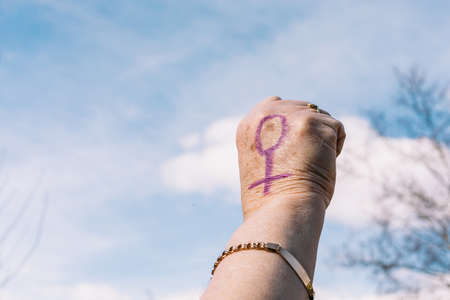 Fist of an older woman with purple painted nails, with the sky in the background, with the female symbol painted. Concept of women's day, empowerment, equality, inequality, activism and protest.の写真素材