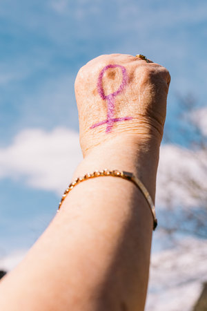 Fist of an older woman with purple painted nails, with the sky in the background, with the female...