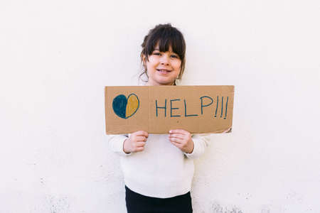 Activist little girl, against the war holds a sign that reads: 'HELP' with the colors of the Ukrainian flag and a yellow flower. Concept of war, confrontation, activism, peace and love.の写真素材