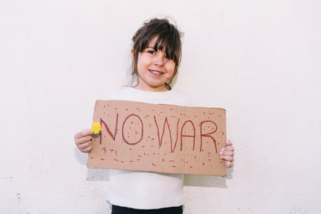 Little girl activist smiling, against the war holds a sign that reads: 'NO WAR' and a yellow flower. Concept of war, confrontation, activism, peace and love.の写真素材