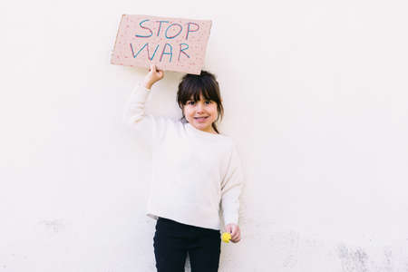 Serious, anti-war activist little girl holding a sign that reads 'STOP WAR' and a yellow flower. Concept of war, confrontation, activism, peace and love.の写真素材