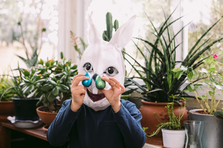 Girl celebrating Easter with a rabbit mask and some chocolate eggs in a glassed-in area surrounded...