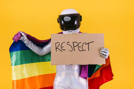 Gay man dressed as an astronaut with a helmet and silver suit, holding a flag of the trans community and a sign that reads: 'RESPECT', on a yellow background.の写真素材