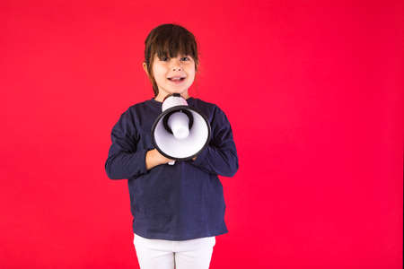 Black-haired girl in a blue sweater and white pants, speaking through a white megaphone, on a red background.の写真素材