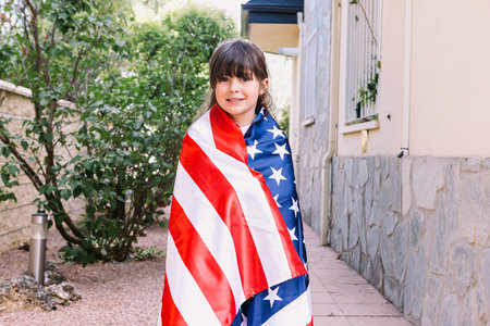 Black-haired girl covered with a large American flag, in the garden of her house. Concept of...