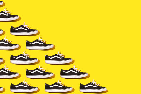 Madrid, Spain - June 21, 2022: Pattern of Vans Old Skool Retro black and white sneakers, on the left side, on yellow background. Skate, surf, fashion, sneaker, modern and retro concept.のeditorial素材