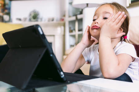 A little blonde girl in front of a tablet, gesturing while watching a video. Concept of childhood, technology, learning, having fun, the Internet and connectivity.の写真素材