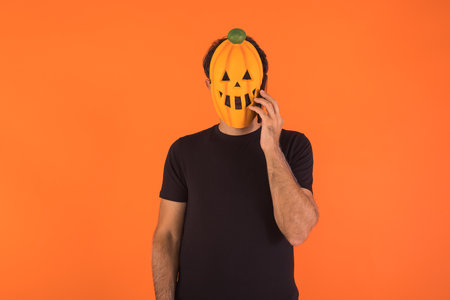 Person with pumpkin mask celebrating Halloween, talking on the mobile, raising his hands. Concept of celebration, All Souls' Day and All Saints' Day.の写真素材