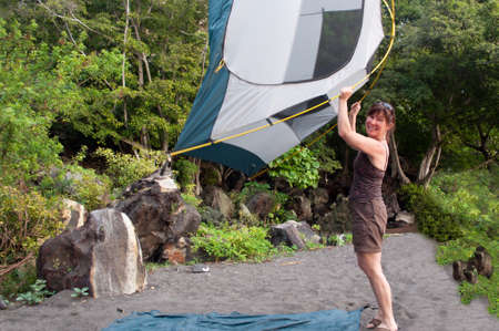 Woman demonstrates how to pitch a lightweight, 2 person tent on a black sand beach campsite.の写真素材