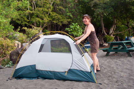 Woman demonstrates how to pitch a 2 person tent on a black sand beach campsite.の写真素材