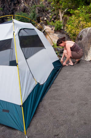 Woman demonstrates how to pitch a 2 person tent on a black sand beach campsite.の写真素材