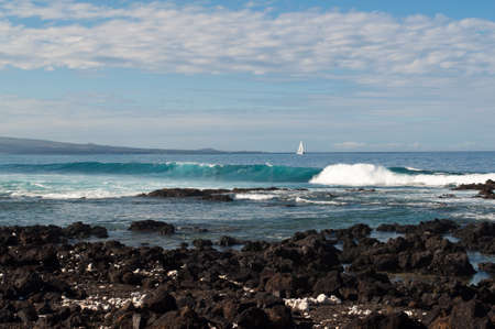 Behind the jewel tone wave sails a ship along the coastline.の写真素材