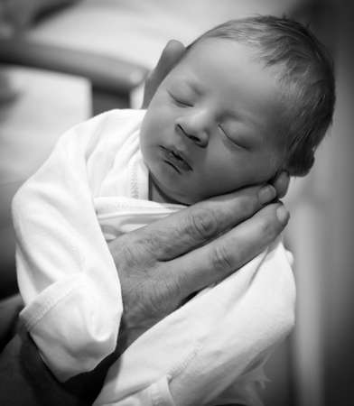 Black and white photo of human hands holding up a sleeping newborn baby.の写真素材