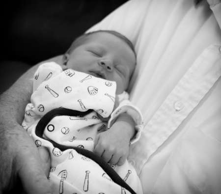 Black and white photo of a sleeping newborn baby being held in human male arms.の写真素材