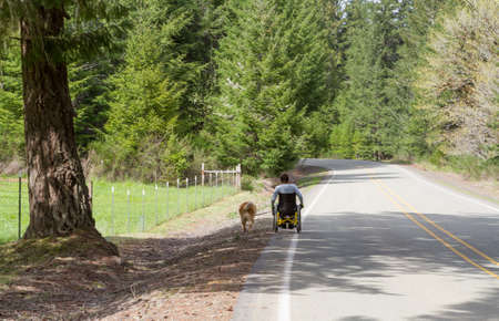 Paraplegic man taking his dog for a walk down a country road.の写真素材