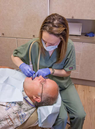 Senior man is getting his teeth checked and cleaned by the dental hygienist at his dentist's office.の写真素材