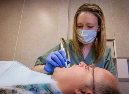 Senior man is getting his teeth checked and cleaned by the dental hygienist at his dentist's office.の写真素材