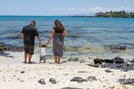 Young parents helping their toddler get his feet wet at the beach.の写真素材