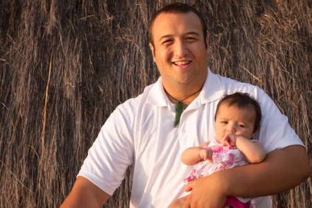 Proud father holding his baby girl in front of a grass hut の写真素材