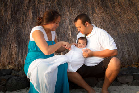 Young couple dressing their baby girl outside a beach hut at sunsetの写真素材