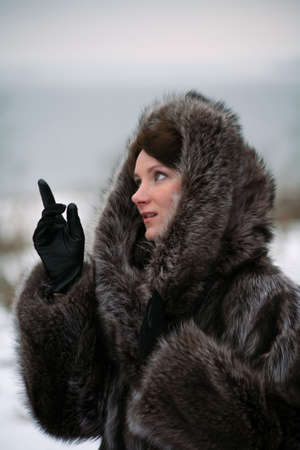 Portrait of a smiling beautiful girl in a fur coat from a raccoon on the natureの写真素材
