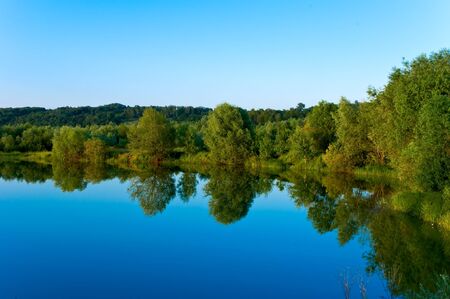 Reflexion of the blue sky and trees in lakeの写真素材