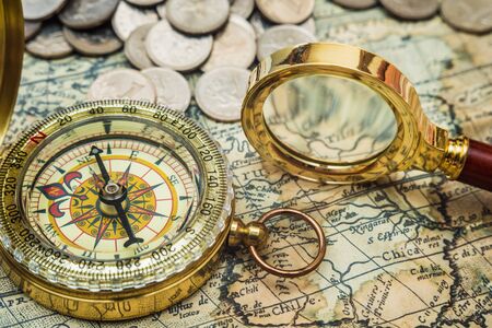 compass and magnifying glass gold color on the old map with coinsの写真素材