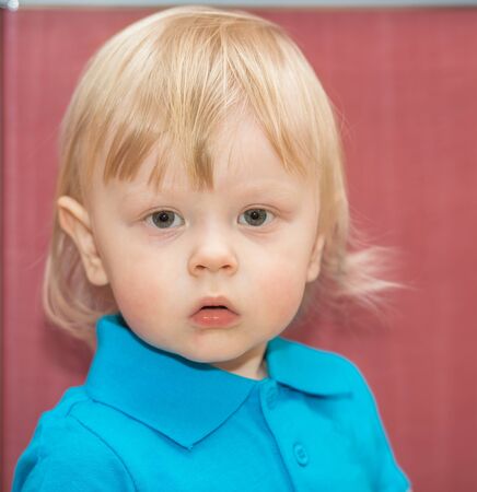 portrait of a little boy in a turquoise t-shirt with a red backgroundの写真素材