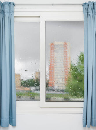 White window with blue curtains on a rainy dayの写真素材