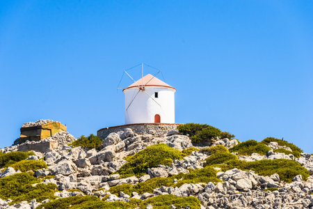 old white windmill on a rocky cliff with vegetation
