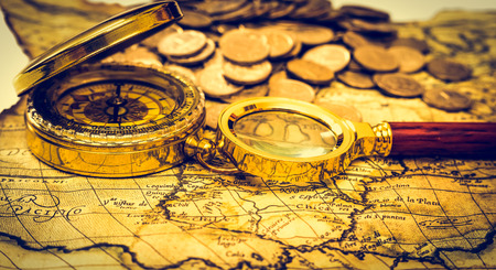 compass and magnifying glass gold color on the old map with coinsの写真素材
